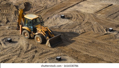 a tractor with a bucket at a construction site levels the soil for pouring the foundation
