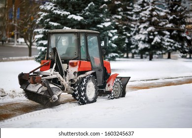 Tractor Cleaning Sidewalk From Snow With Snow Plow And Rotating Brush. Municipal Service Removing Snow, Sprinkle Salt And Sand To Prevent Slipping On Road. Vehicle With Brush And Scoop Remove Snow