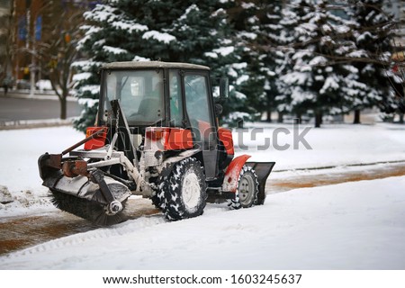 Tractor cleaning sidewalk from snow with snow plow and rotating brush. Municipal service removing snow, sprinkle salt and sand to prevent slipping on road. Vehicle with brush and scoop remove snow