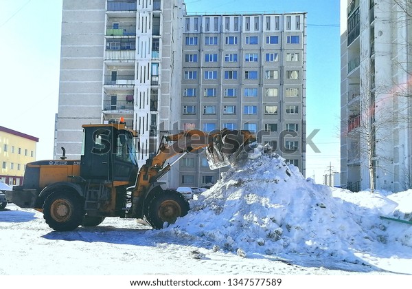 Tractor cleans snow in the yard and collects a\
pile, Surgut, Russia - March 24,\
2019