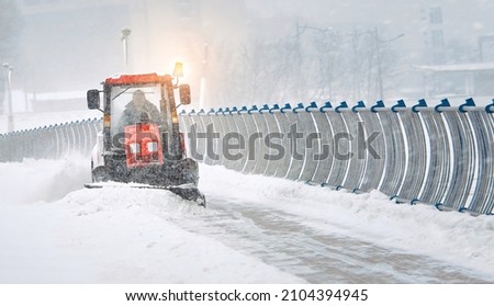 Tractor clear snow from pedestrian zone on car bridge, sidewalk snow management in the city during blizzard. Snow plow service clearing road from snow during snowstorm. Road maintenance in winter
