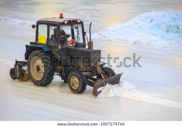 The tractor clears the ice on the\
road of the stadium for races from snow and\
unevennesses.