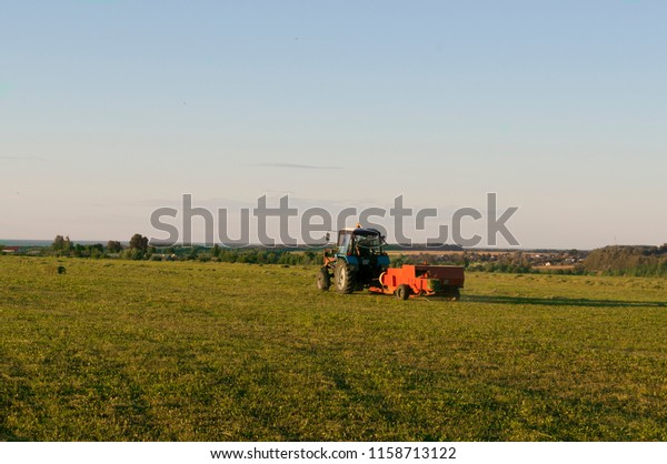 The tractor collects the hay in sheaves and\
takes it off the field after the mowing of the grain.\
Agroindustrial industry.