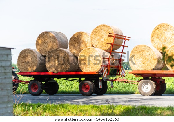 A tractor drives with two trailers and some hay\
bales on a  country road
