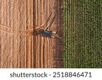 A tractor is driving through a field of corn. The field is mostly brown with some green in the background