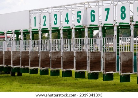 tractor and empty open transportable starting gate with a number of stalls on the racetrack grounds
