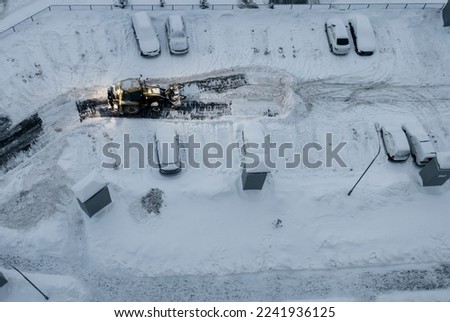 Tractor loader machine uploading dirty snow into dump truck. Cleaning city street, removing snow and ice after heavy snowfalls. Snowplow clean pavement sidewalk road driveway