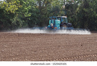 Tractor With A Long Boom Sprayer Sprays Pesticides On A Just Plowed Field 