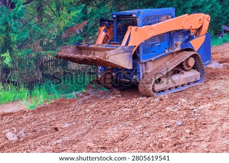 Tractor machine moves dirt on forest trail while trees surround construction area.