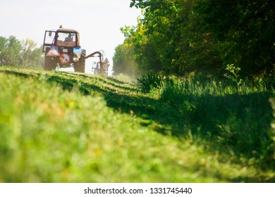Tractor with a mechanical mower mowing grass on the side of the asphalt road. Road improvement road services. Cleaning of adjacent areas.