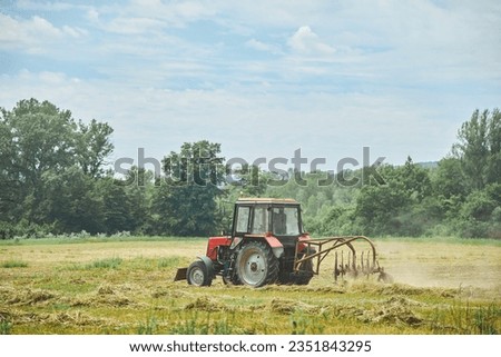 The tractor mows and cleans the grass in the field. Harvesting hay for animal feeding