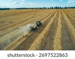 A tractor operates in a large field, creating hay bales during the summer harvest.