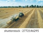 A tractor operates in a large field, creating hay bales during the summer harvest.