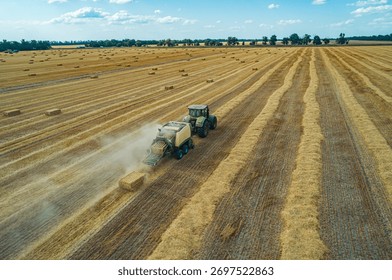 A tractor operates in a large field, creating hay bales during the summer harvest.