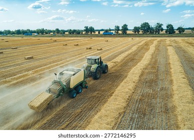 A tractor operates in a large field, creating hay bales during the summer harvest.