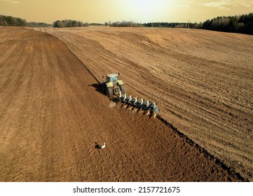 Tractor with plow on field cultivating. Green tractor plowing field on sunset. Cultivated land and soil tillage. Agricultural tractor on field cultivation. Tractor disk harrow on plowing, aerial view.