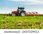 Tractor with plowing equipment preparing the soil in a green field under a clear sky