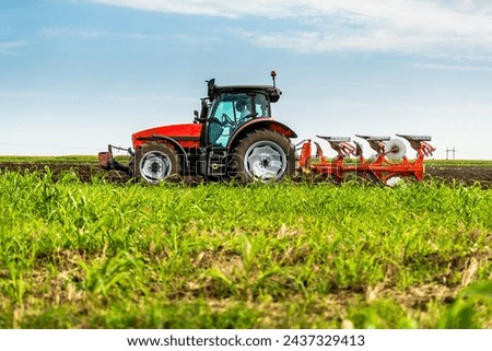 Tractor with plowing equipment preparing the soil in a green field under a clear sky