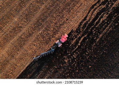 Tractor Plowing field on sunset. Red Tractor with Plough on Plowed. Ploughing and Soil Tillage. Agricultural Tractor on Cultivation Field for Sowing Seeds. Big Tractor During Field Cultivating. 
