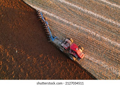 Tractor Plowing field. Red Tractor with Plough on Plowed. Ploughing and Soil Tillage. Agricultural Tractor on Cultivation Field for Sowing Seeds. Big Tractor During Field Cultivating. 
