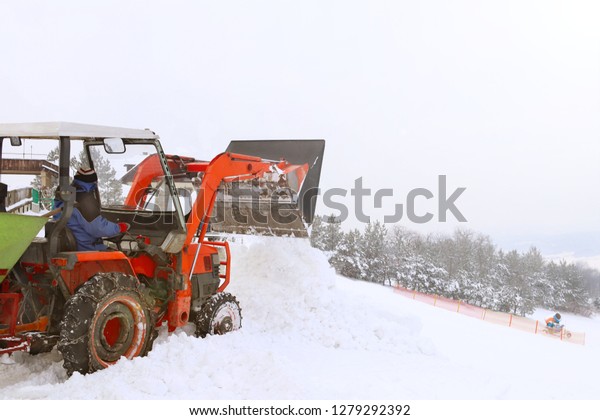The tractor pours snow with his bucket on the ski\
slope. The work of the snowcat in the winter time. Preparation of\
the sports ground for competitions. Snow drifts and mechanization\
in working with