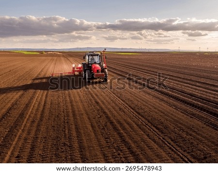 Tractor pulling a planter machine across a plowed field, seeding crops under a cloudy sky