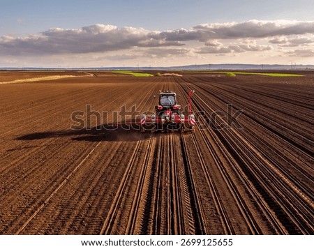 Tractor pulling a planter machine sowing seeds in a rural cultivated field
