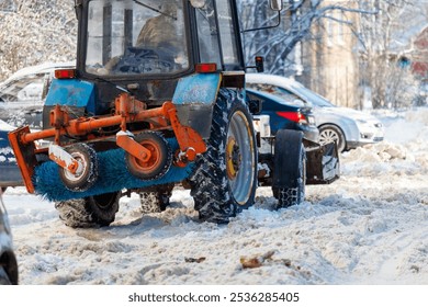 A tractor is pulling a snow plow behind it. The snow plow is attached to the back of the tractor. The tractor is parked in front of a car
