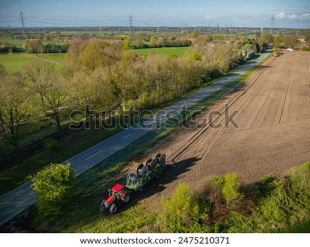 Tractor pulling a trailer with four wire spools, cable drums. Deploying cables or wires over larger distances. Installing optical fiber cables along trench. Rolling out fiber optic cables for network