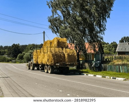 Tractor pulling a trailer loaded with large square hay bales on an asphalt road in a rural area