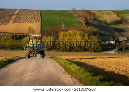 Tractor returning from spraying crops, fields, golden hour, earth, blooming trees in spring colors, furrows of agricultural land. Concept of the problem of barren land, decreasing yields