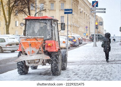 Tractor with salt spreader in winter day during snow storm, tractor spreading rock salt, sand on sidewalk, winter road maintenance, prevent slipping.Tractor de-icing street, melt ice and snow - Shutterstock ID 2229321475