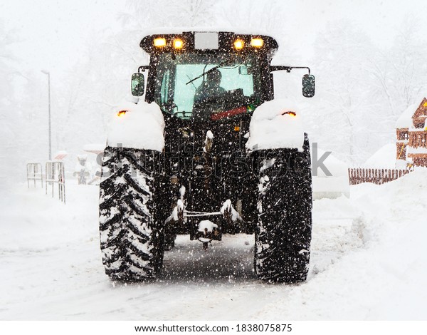 Tractor shovels snow from the road\
during heavy snowfall. Cleaning for cars and pedestrians\
