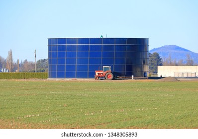 A Tractor Sits Parked In Front Of A Huge Livestock Manure Storage Tank On A Local Farm. 