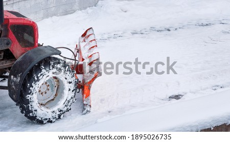 Tractor with snow plow blade clears road in city from fresh fallen snow. Snowplow removing snow on street after blizzard. Snowplow vehicle clears snowy road during blizzard. Snow clearing equipment
