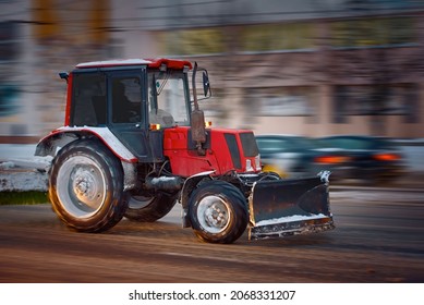 Tractor With Snow Plow Riding On Night Snowy Road. MOTION BLUR. Road Maintenance At Winter Season, Cleaning Road At Night. Heavy Machinery Working On City Street During Snow Storm