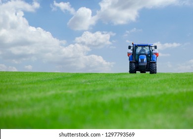 Tractor spreading fertilizer on crops in farm field against blue sky