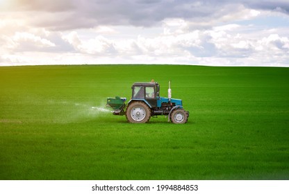Tractor spreading potash fertilizer on green wheat field. Agriculture vehicle spraying field. Tractor spray fertilizers on green field, agriculture wallpaper. Farmer spreading potash fertilizers.