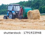 A tractor with a trailed bale making machine collects straw rolls in the field and makes round large bales