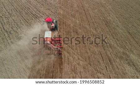 Tractor with a unit processes dusty soil on the prairie. Farmer sows in arid, lifeless steppes. Concept of risky agribusiness. Aerial view