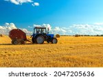 A tractor uses a trailed bale machine to collect straw in the field and make round large bales. Agricultural work, baling, baler, hay collection in the summer field.