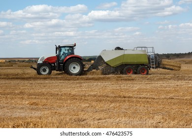 Tractor with wheat straw baling machine working on a harvested wheat field with bales and straw dust in the air