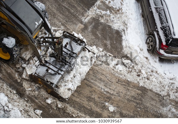 tractor-excavator removes snow in the\
city yard in the Parking lot. winter. work of public\
utilities