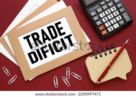 TRADE DEFICIT red background with notepad and calculator. text on white paper.