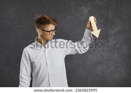 Trader or business owner who lost money holding graph chart arrow pointing down isolated on grey background. Unhappy young man experiences profit decrease, budget cuts, devaluation or poor performance