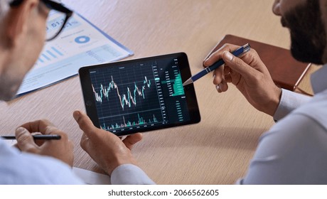 Trader consulting business investor showing crypto trading chart using digital tablet computer analyzing stock exchange market discussing risks and investment financial profit. Over shoulder view