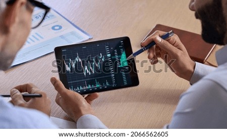 Trader consulting business investor showing crypto trading chart using digital tablet computer analyzing stock exchange market discussing risks and investment financial profit. Over shoulder view