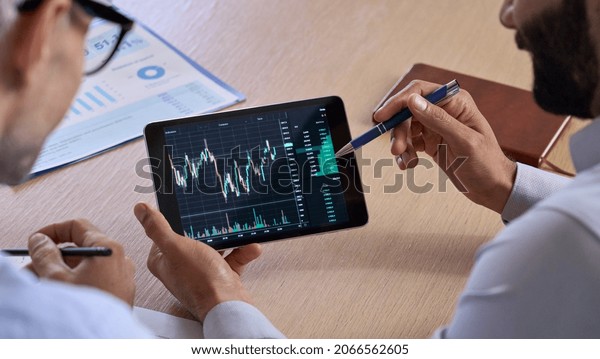 Trader consulting business investor showing crypto\
trading chart using digital tablet computer analyzing stock\
exchange market discussing risks and investment financial profit.\
Over shoulder view
