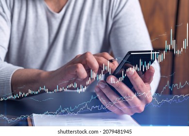 Trader holding in the hands a smart phone and researching stock market to proceed right investment solutions. Internet trading and wealth management concept. Hologram Forex chart over close up shot.
