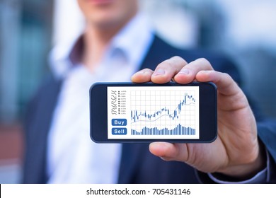 Trader showing smartphone screen with trading interface dashboard with candlestick chart, quotes and buy sell buttons, stock exchange and fintech concept